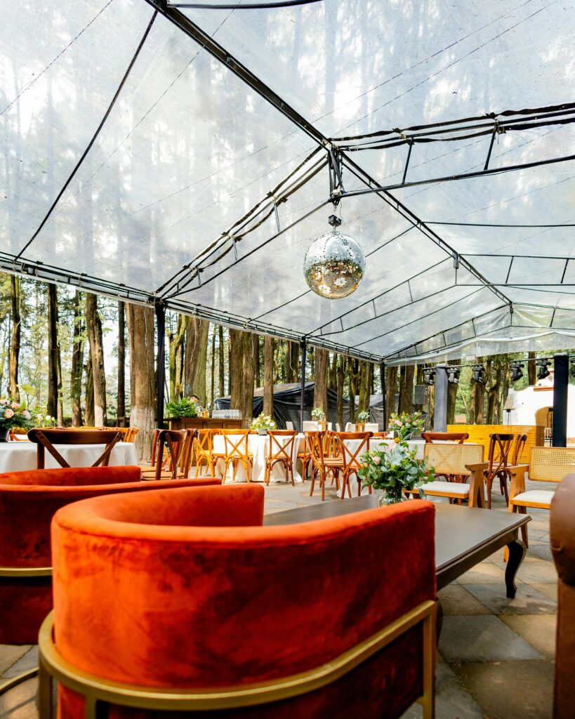 Elegant outdoor venue with a clear ceiling and luxurious seating amidst trees.